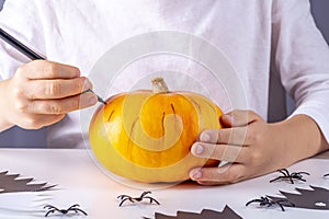 Happy halloween. Child hand draws face on pumpkin with marker  . Funny handmade paper ghost, spiders toy on white background.