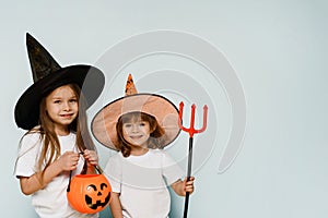 Happy Halloween. Cute girls in witch hats and with a bucket in the form of a pumpkin are ready to collect sweets for