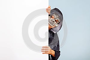 Happy Halloween! Cute little boy in a costume hiding behind white banner blank. Happy kid holding cardboard background with copy