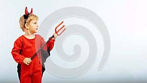 Happy Halloween! Cute little boy in devil halloween costume with horns and trident on light blue background