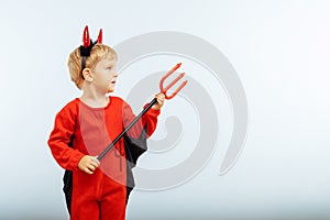 Happy Halloween! Cute little boy in devil halloween costume with horns and trident on light blue background