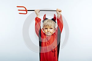 Happy Halloween! Cute little boy in devil halloween costume with horns and trident on light blue background