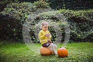 Happy Halloween. Cute little girl is sitting on a pumpkin and holding an apple in her hand