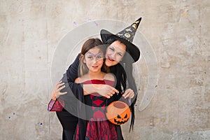 Happy halloween. Cute young woman and girl dressed as witches on grey background hold pumpkin to collect candy and sweets at