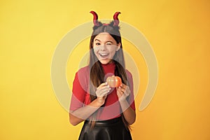 happy halloween. devil kid with pumpkin. trick or treat. teen girl on yellow background.