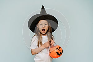 Happy Halloween. A frightened girl in a witch& x27;s hat and with a bucket in the form of a pumpkin says wow. Copy space