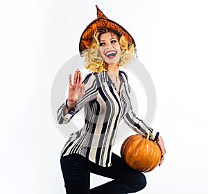 Happy Halloween girl in witch hat with pumpkin waving hand. Smiling female witch with magic pumpkin. Happy Halloween