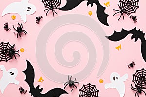Happy Halloween greeting card design. Frame made of bats, ghosts, spiders, webs on pastel pink background. Flat lay, top view,