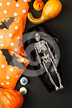 Happy Halloween holiday concept. Decorative skeleton of man in paper handmade coffin and traditional candy bags on black