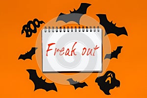 Happy halloween holiday concept. Notepad with text Freak out on white and orange background with bats, pumpkins and ghosts