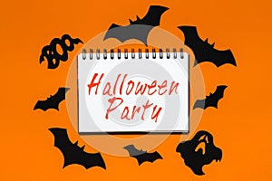 Happy halloween holiday concept. Notepad with text Halloween party on white and orange background with bats, pumpkins and ghosts