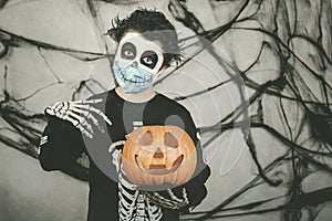 Happy Halloween.kid wearing medical mask in a skeleton costume with halloween pumpkin photo