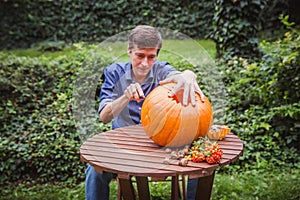 Happy halloween. Man carving big pumpkin on a wooden table for Halloween outside. Close-up photo