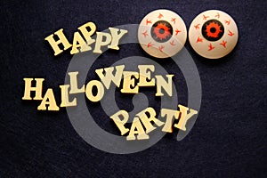 HAPPY HALLOWEEN PARTY and two balls of eye on a dark blue background. Words of wooden letters. Decoration for the holiday.