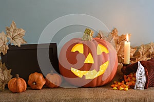 Happy Halloween Pumpkin with decorations, candy corn and frame for text, all on rustic burlap table and blue textured background w