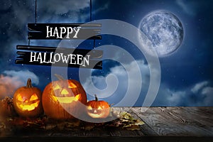 Happy Halloween. Spooky pumpkin jack o`lanterns on wooden table under full moon