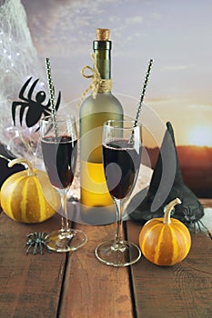 Happy Halloween, still life with red wine cocktail, pumpkins, spiders and cobwebs, illumination, against the backdrop of a landsca