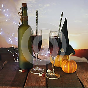 Happy Halloween, still life with red wine cocktail, pumpkins, spiders and cobwebs, illumination, against the backdrop of a landsca