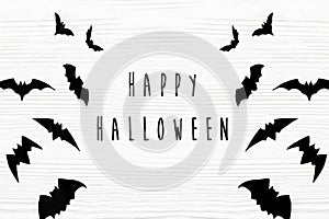 Happy Halloween text, greeting card flat lay. Black bats on white wooden background. Modern minimal halloween paper diy