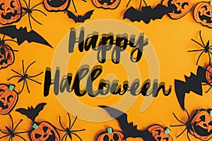 Happy Halloween text sign on modern pumpkins, jack o lanterns, spiders, bats frame flat lay on orange background. Season`s
