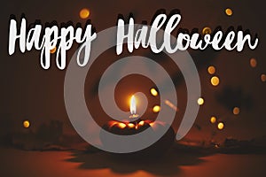 Happy Halloween text sign on pumpkin candle burning on dark orange background with lights and flying black bats. Season`s greetin