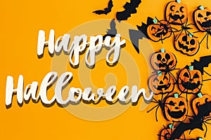 Happy Halloween text sign on pumpkins, jack o lanterns, spiders, bats border flat lay on orange background. Season`s greeting car