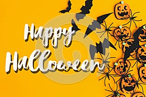 Happy Halloween text sign on pumpkins, jack o lanterns, spiders, bats border flat lay on orange background. Season`s greeting car