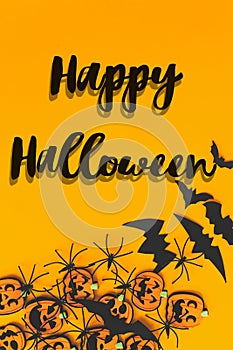 Happy Halloween text sign on pumpkins, jack o lanterns, spiders, bats border flat lay on orange background. Season`s greeting car