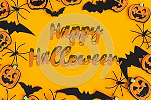 Happy Halloween text sign on pumpkins, jack o lanterns, spiders, bats frame flat lay on orange background. Season`s greeting card