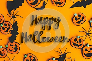 Happy Halloween text sign on pumpkins, jack o lanterns, spiders, bats frame flat lay on orange background. Season`s greeting card