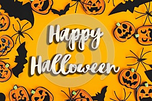 Happy Halloween text sign on pumpkins, jack o lanterns, spiders, bats frame flat lay on orange background. Season`s greeting card