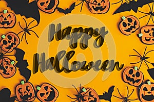Happy Halloween text sign on pumpkins, jack o lanterns, spiders, bats frame flat lay on orange background. Season`s greeting card