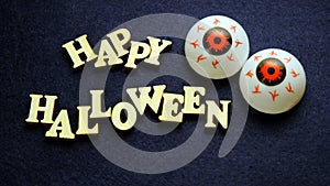 HAPPY HALLOWEEN and two balls of eye on a dark blue background. Words of wooden letters. Emotional decoration for the holiday.