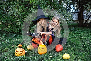 Happy Halloween. Two funny children in witch suits and with pumpkins sitting outdoor