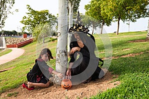 Happy halloween. Young beautiful woman and girl dressed as witches next to a tree and with a pumpkin to collect candy and sweets.