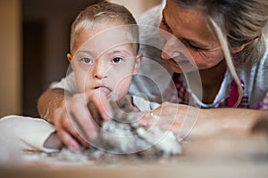 A happy handicapped down syndrome child with his mother indoors baking.