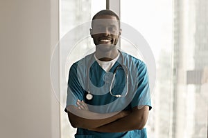 Happy handsome African American surgeon in blue scrubs standing indoors