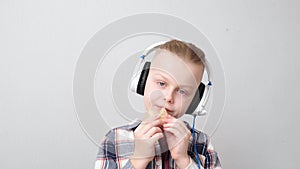 Happy handsome boy with headphones listening music and eating on a gray background. Relax with tunes.