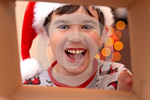 A happy, handsome Caucasian boy in a New Year`s jumper and a Santa Claus hat smashes into a box