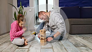 Happy handsome father and happy daughter play game with wooden tower blocks bricks