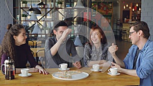 Happy handsome guy is telling funny story to his friends while dining in cafe while his mates are laughing and doing