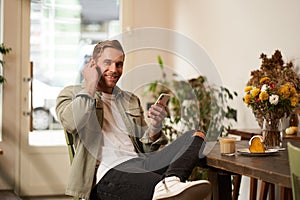 Happy handsome man in coffee shop, listening to music in wireless earphones, connects to cafe wifi to enjoy favourite