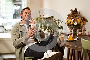 Happy handsome man in coffee shop, listening to music in wireless earphones, connects to cafe wifi to enjoy favourite