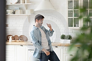 Happy handsome man dancing to music alone at kitchen.