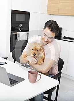 Happy handsome man hugs his pet dog Norwich Terrier and working on laptop at home