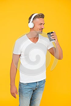 Happy handsome man listen to music in earphones drinking takeaway coffee cup, break time