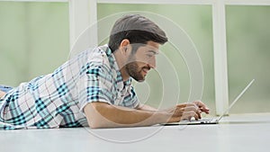 happy handsome man lying down on floor using laptop computer at home