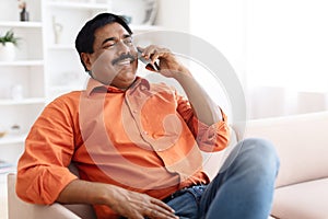 Happy middle aged indian man talking on phone at home