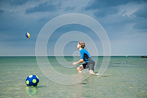 Happy handsome teen boy running and playing with ball in neoprene swimsuit in sea