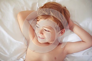 Happy handsome toothy smiling child boy lying bed and resting.